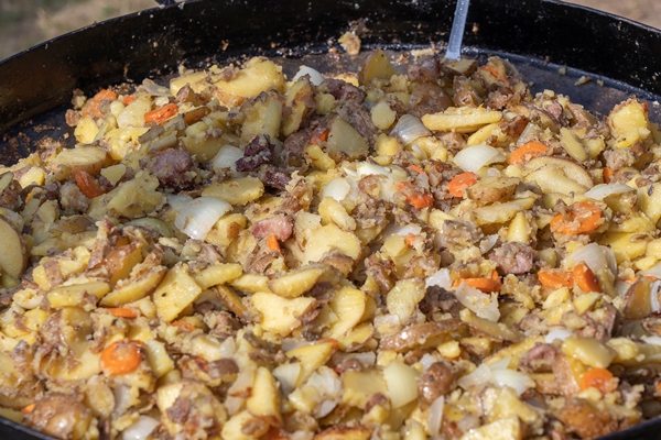roast potatoes carrots onions and meat in a large pan delicious food at the festival field kitchen at the hearth young potatoes are fried in oil street food ukraine - Крошенка фронтовая
