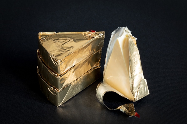 thre triangular pieces of melted cream cheese wrapped in a golden aluminium foil and without packaging on a black background portioned triangular cheeses - Горячие бутерброды "Ленивые драники"