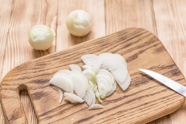 sliced onions with half rings on a wooden chopping board on a wooden background - Жареный картофель с луком