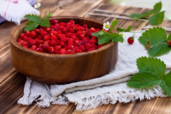 a wooden bowl of red ripe wild strawberries and flowers on an old wooden surface - Варенье из лесной земляники