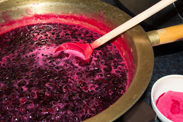 at home black currant jam is cooked in a copper basin and mixed with a wooden spoon - Желе из красной смородины