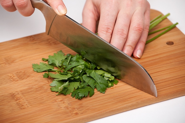 hand with a kitchen knife cuts and chops parsley on a wooden cutting board - Суп "Шашлычный" на костре