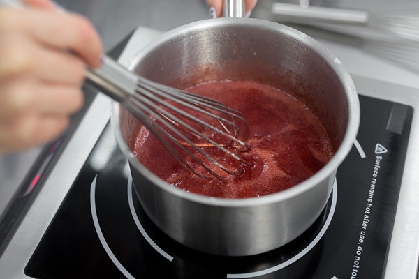 pastry chef cooks strawberry puree with sugar in a saucepan - Леденцы на палочке