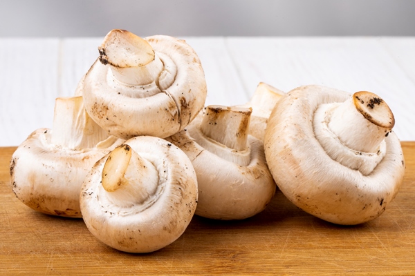 side view of fresh mushrooms champignon on wooden board on white background - Сбор, заготовка и переработка дикорастущих плодов, ягод и грибов