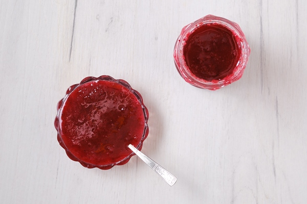 top view of jar and saucer with cherry jam on white wooden background - Мандрики с вишней