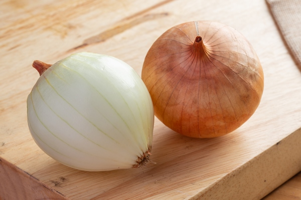 two onions on a light brown wood cutting board - Пшеничная каша в котелке на костре