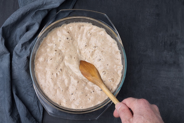 a man s hand checks the readiness of the homemade sourdough for making rye bread with a wooden spoon - Постный маковый рулет с мёдом и изюмом