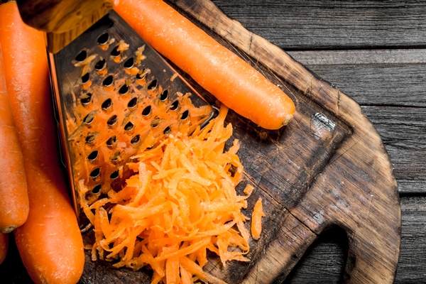 grated carrots on a cutting board with a grater on wooden table - Закуска из фасоли с овощами по-гречески