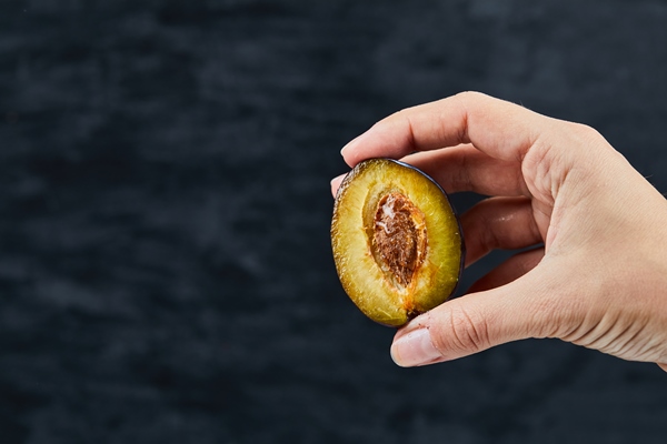 hand holding a half cut of plum on black - Сливово-имбирный джем
