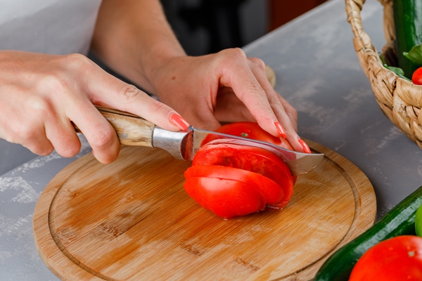 woman slicing tomato on a cutting board high angle view on a gray surface - Пицца из кабачков
