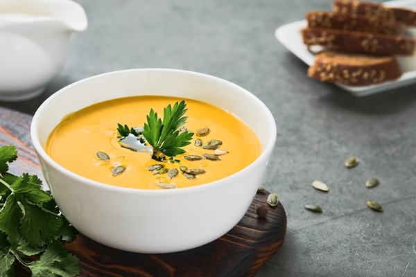 pumpkin and carrot chowder with olive oil in a white cup pumpkin seeds and parsley on a gray background close up on seasonal vegetarian soup selective sharpening on parsley - Постный тыквенный суп "Копатыч"