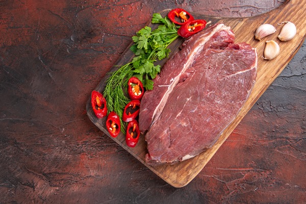 above view of red meat on wooden cutting board and garlic green chopped pepper on dark background - Королевский суп-пюре