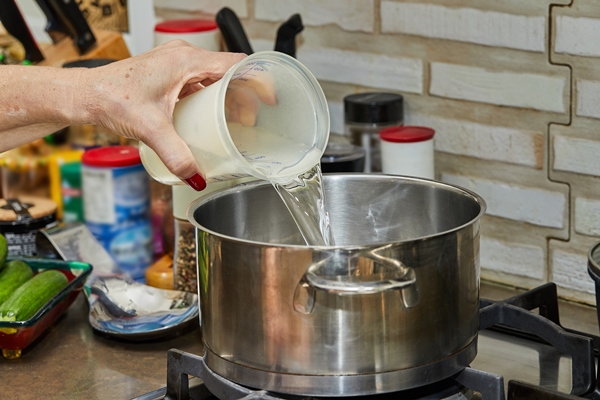 chef pours water from measuring cup into pot ongas stove - Старинные секреты приготовления мясных бульонов