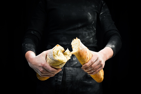 women s hands break the baguette isolated on black background - Королевский суп-пюре