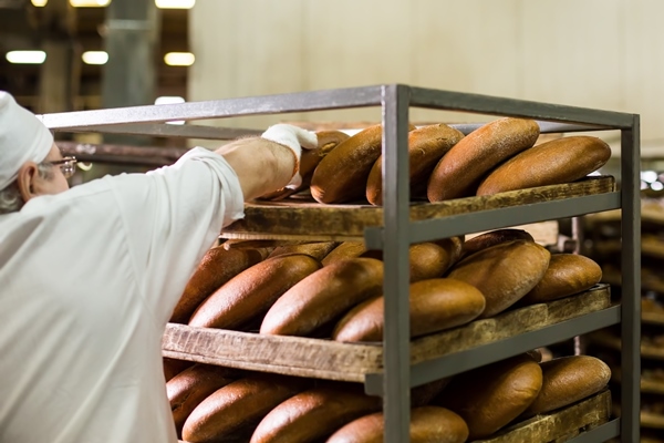 worker at bread factory rack with freshly baked bread - Ржаной кислый хлеб