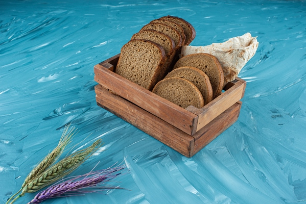 a wooden box full of sliced brown fresh bread with wheat ears on blue surface - Пеклеванный хлеб