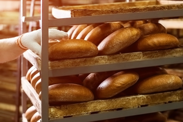 brown bread loaves on rack hand touching bread on shelves big scale of production baked goods made f - Пеклеванный хлеб