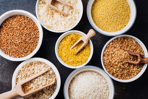 variety of cereal flakes rice millet buckwheat oatmeal superfood in white ceramic bowls on dark old concrete background top view - Углеводная питательность рациона