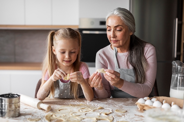 cheerful caucasian little granddaughter and old grandmother smeared with flour make cookies from dough together - Сибирские пельмени
