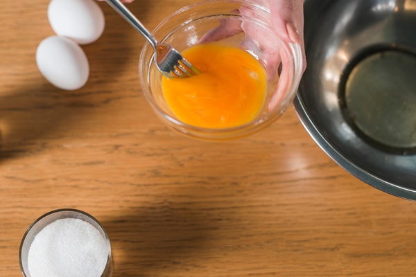close up of woman s hand mixing the egg yolk with fork in the glass bowl - Блинцы яичные простые на воде