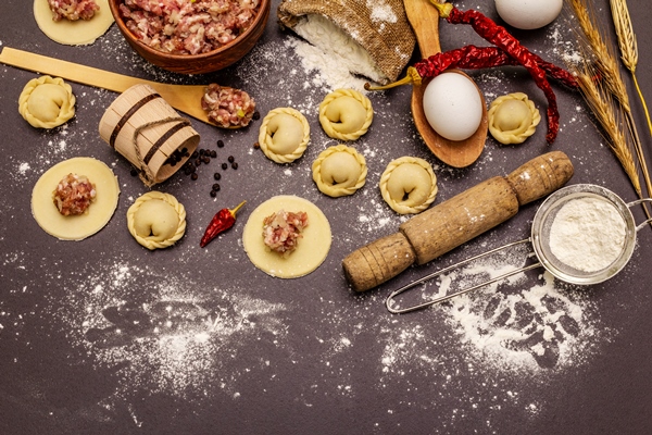 composition with raw dumplings and ingredients on trendy black stone concrete background process of cooking - Пельмени