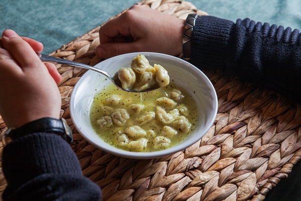 from above dushpara with spoon and human hand in plate - Пельмени