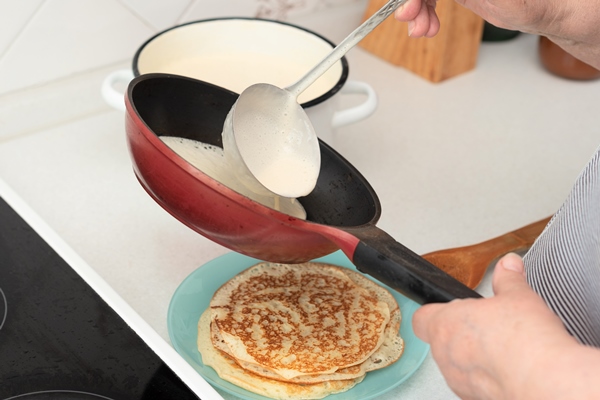 senior woman chef pour portion of liquid dough by hands with ladle on frying pan for baking pancakes 1 - Блинцы яичные простые на воде