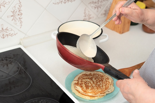 senior woman chef pour portion of liquid dough by hands with ladle on frying pan for baking pancakes - Блинцы тонкие заварные на кефире и яйцах