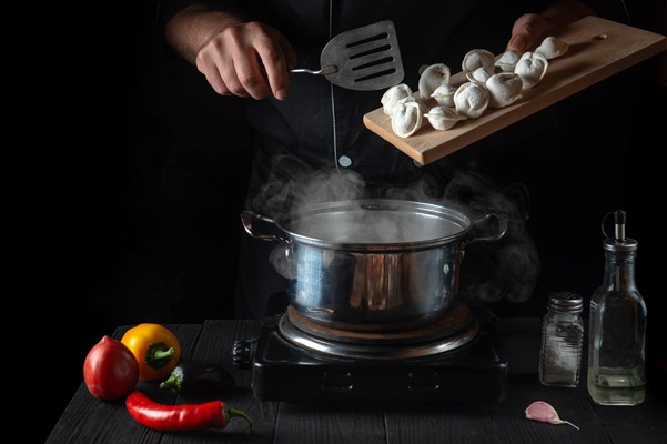 the chef cooks meat dumplings in a saucepan in the restaurant kitchen - Сибирские пельмени