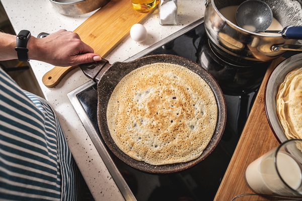 woman is standing at the stove and frying pancakes in a hot pan - Блинцы-скородумки
