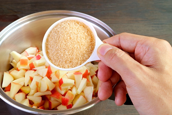 hand adding a cup of unrefined sugar into the pot of diced fresh apples for making apple compote - Яблочная пастила