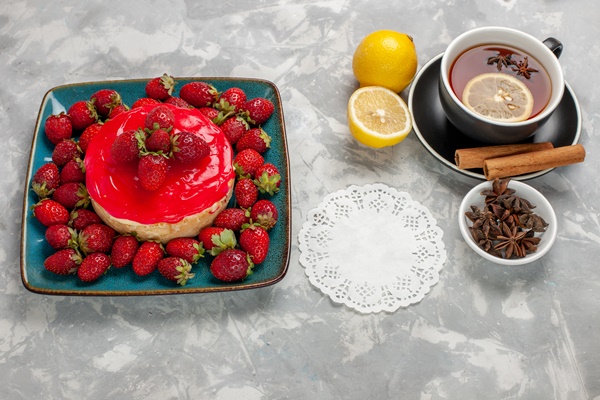 front view delicious looking cake little pie with cup of tea and fresh strawberries on white surface - Клубнично-молочное желе