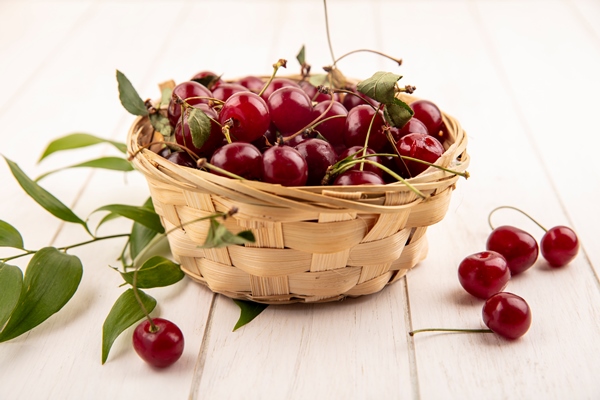 side view of cherries in basket with leaves on wooden background - Компот из яблок и вишни (школьное питание)