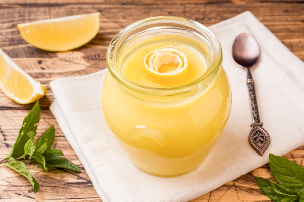 homemade lemon curd in glass jars with fresh lemons rustic wooden background - title=