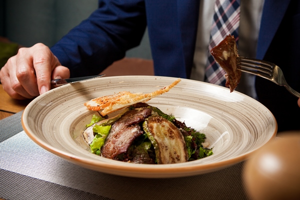 side view fried meat with fried zucchini and crackers and human hand and fork in round plate - Банкет