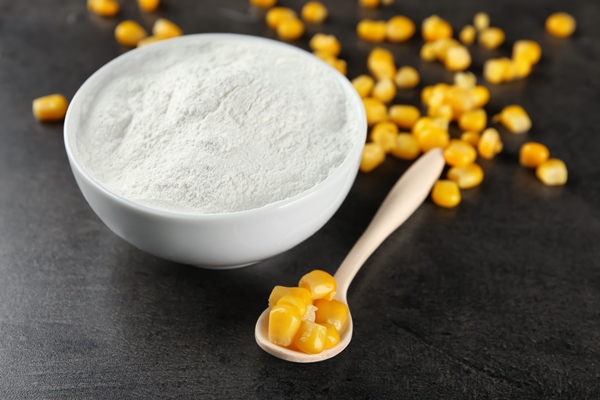 spoon with kernels and corn starch in bowl on table - title=