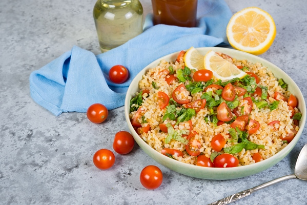 tabouleh salad with tomatoes fresh herbs plate is left frame concrete - Салат Табуле с помидорами и зеленью