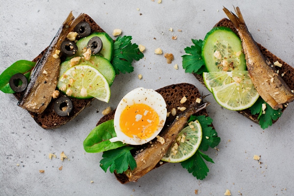 fish sandwiches with sprats cucumber lime boiled eggs parsley leaves mango rye bread gray old concrete surface selective focus - Бутерброды со шпротами