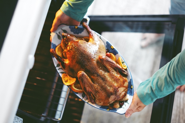 woman cooking duck with vegetables puting it from oven - Святочные традиции: гусь с кислой капустой