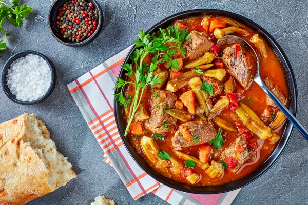 close up overhead view delicious beef okra stew served bowl with spoon grey concrete table with ciabatta bread flat lay - Чахохбили из баранины