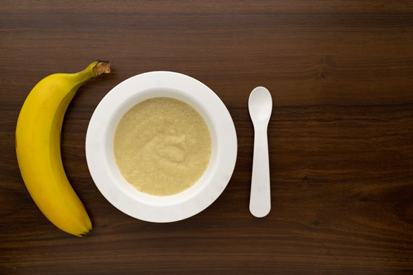 plastic bowl with porridge baby wooden background - Банановое пюре для детей до 1 года