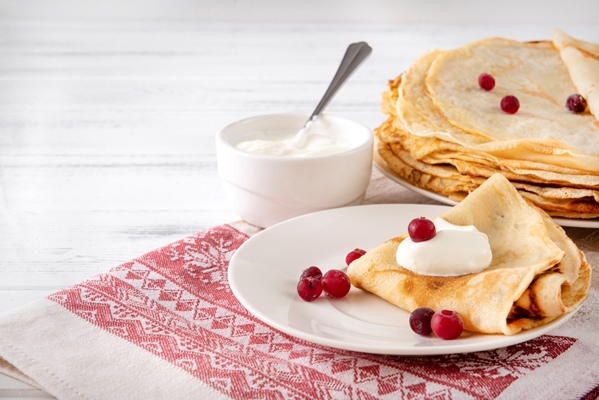 russian pancakes with berries sour cream plate towel with red pattern white surface - Боярские блинцы на сливках