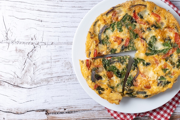 ital anskaa frittata so spinatom pomidorami lukom i percem na belom derevannom stole - Запеканка с крапивой