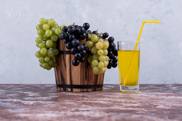 grozd zelenogo i krasnogo vinograda v vedre i stakan soka - Натуральный виноградный сок