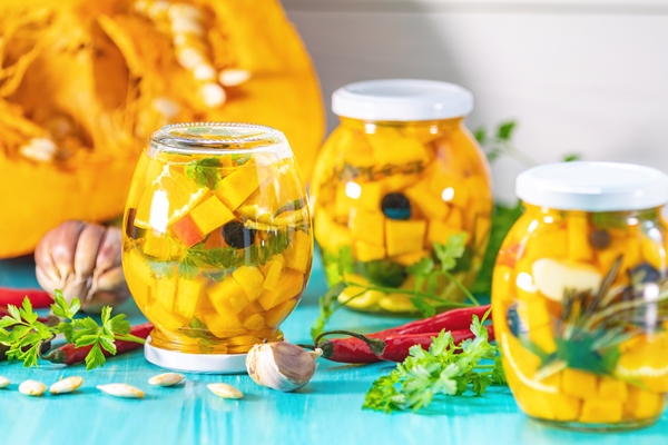 marinovannye konservnye banki domasnie apel sinovye ogurcy iz tykvy s krasnym ostrym percem cili svezie specii petruski na svetlo biruzovom derevannom fone fermentirovannye produkty - Маринованная тыква с лимоном перцем и оливками