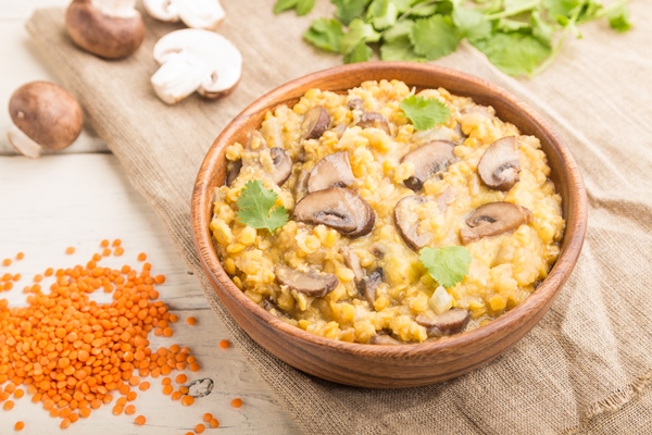 kasa iz cecevicy s sampin onami i koriandrom v derevannoi miske na beloi derevannoi poverhnosti vid sboku vyborocnyi fokus - Красная чечевица с грибами